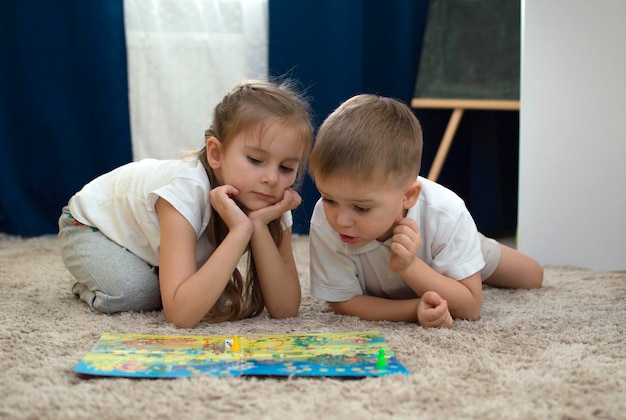 Portrait of two children lying on the floor and playing the board game walker in the nursery. A board game and the concept of children's leisure. Selective focus.