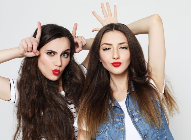 Portrait of two cute playful women showing horns with fingers on head