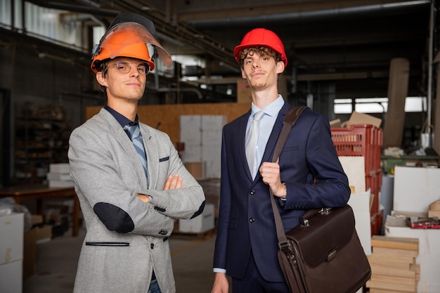 Portrait of two engineers in the factory successful people elegantly dressed wearing protective helmets