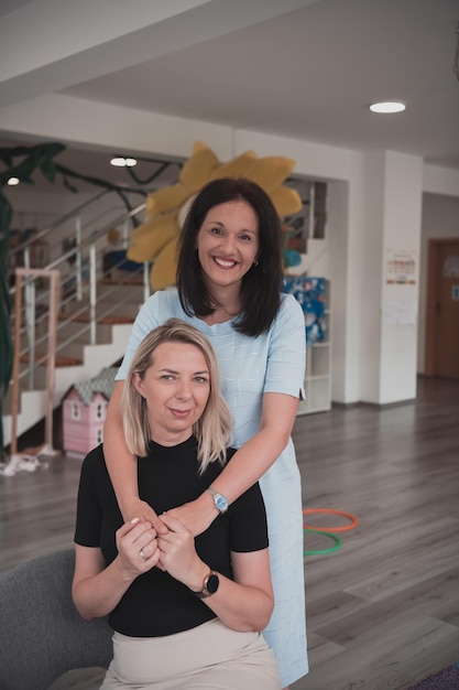 Portrait of two hugging female teachers in a preschool institution in the background of the classrooms