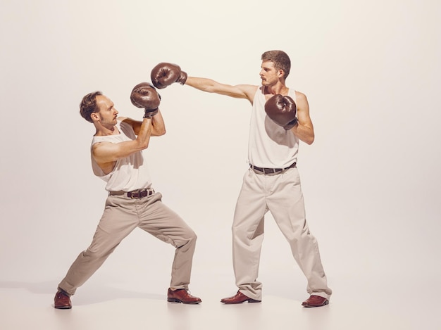 Portrait of two men playing boxing in gloves isolated over grey studio background funny image of two