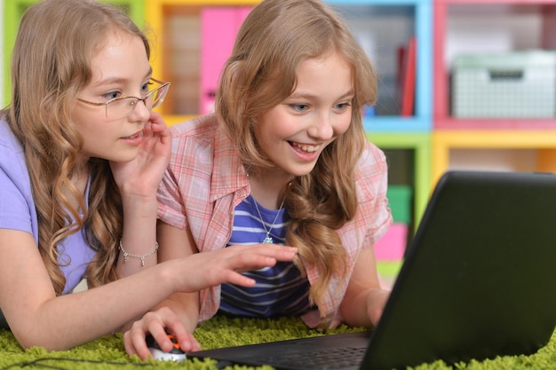 Portrait of two pretty little girls lying on floor and using laptop