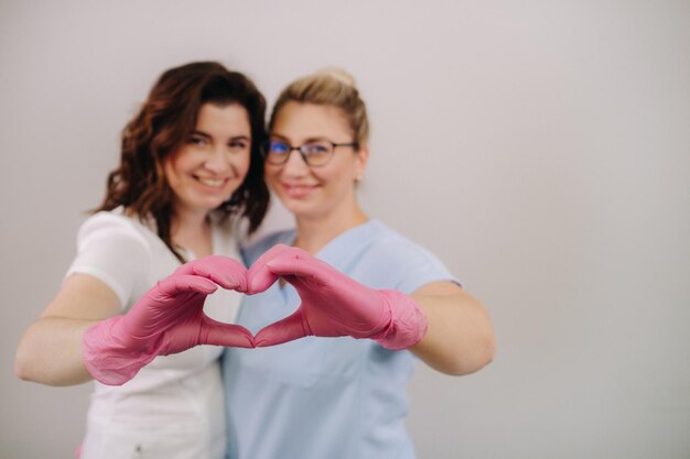 Portrait of two qualified cosmetologistswomen confidently smiling and making a heart with their hands in a medical center