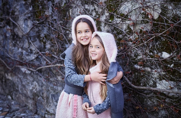 Portrait of two sweet girlfriends posing outdoor on grey natural rock background.