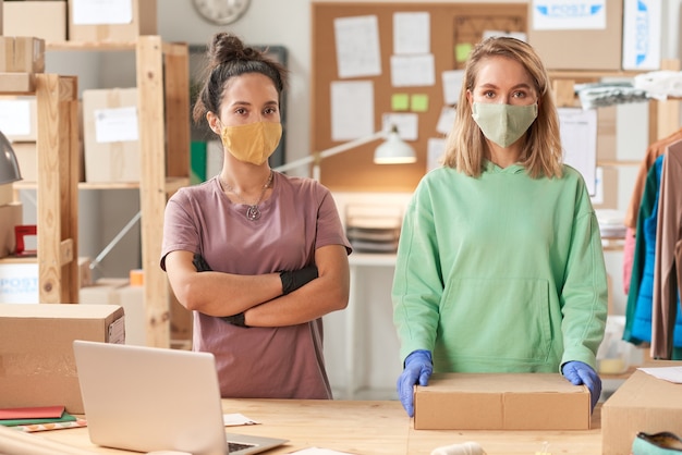 Portrait of two women in masks looking at front working in delivery service