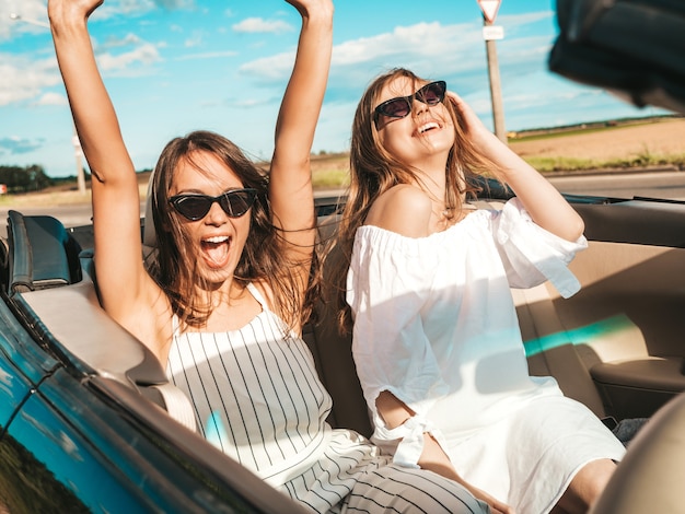 Portrait of two young beautiful and smiling hipster female in convertible car