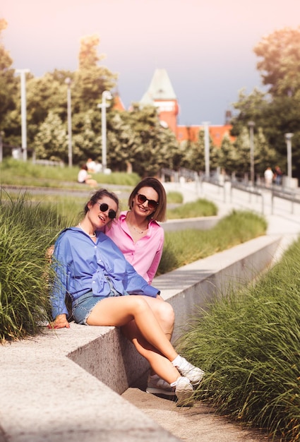 Portrait of two young beautiful smiling hipster female in trendy summer color clothes carefree women posing on river background Positive models having fun hugging