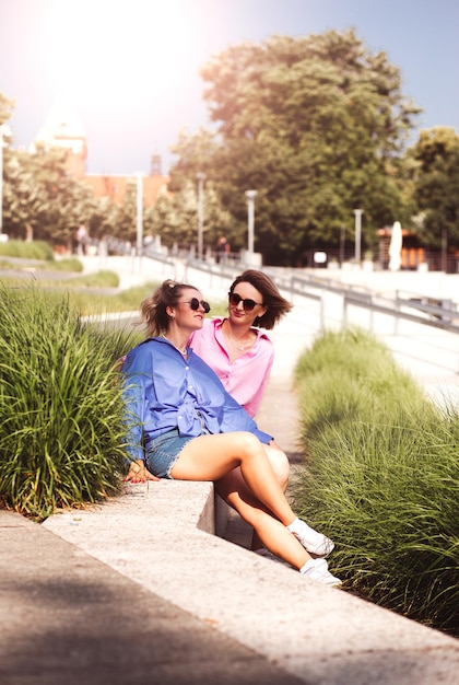 Portrait of two young beautiful smiling hipster female in trendy summer color clothes carefree women posing on river background Positive models having fun hugging