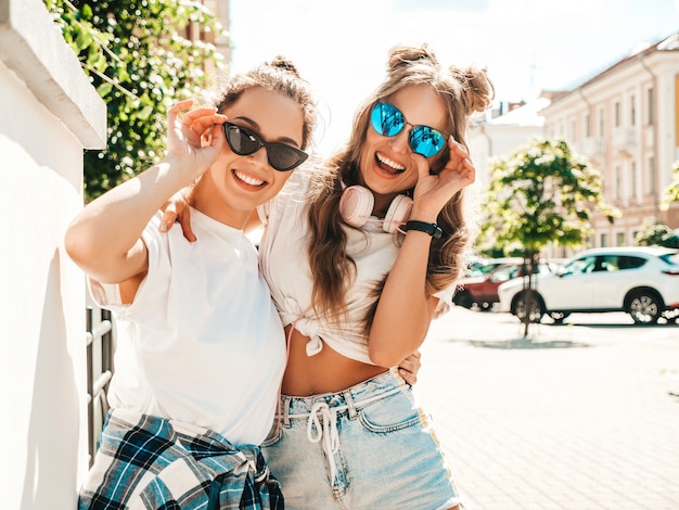 Portrait of two young beautiful smiling hipster girls in trendy summer white t-shirt clothes