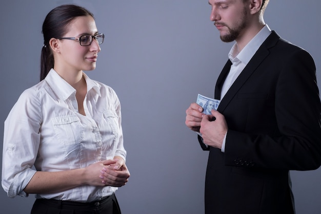 Portrait of two young businessmen in business clothes. A business woman with glasses watching a man take out a press of dollar bills from his jacket pocket.