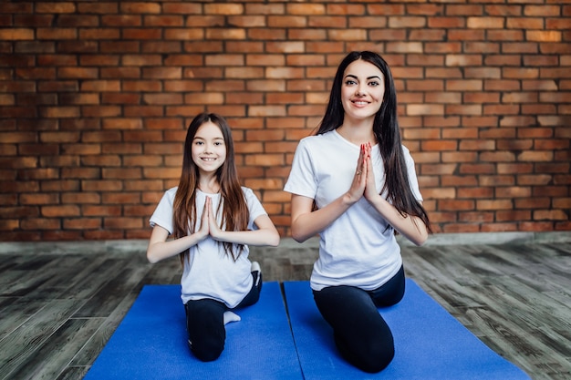 Portrait of  two young flexible girls  sitting on yoga mat and preparing before training.At yoga center.