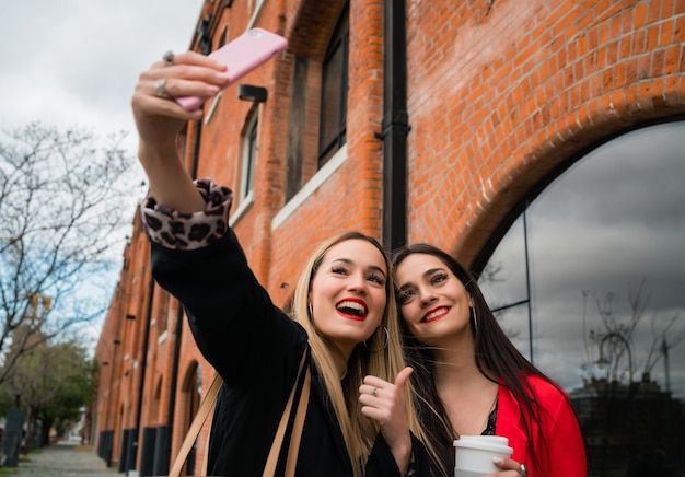 Portrait of two young friends taking a selfie with mobile phone at the street. Lifestyle and friendship concepts.