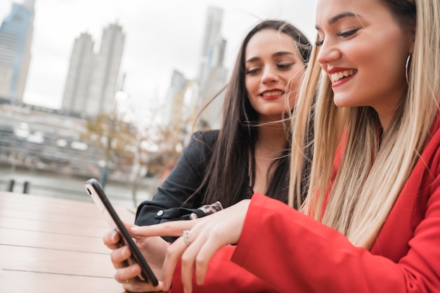 Portrait of two young friends using their mobile phone while sitting at coffee shop. Lifestyle and friendship concept.