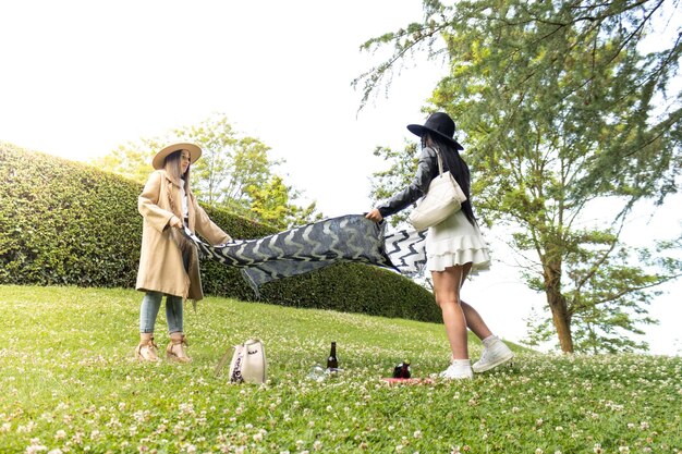 Portrait of two young girls spreading out a blanket on the ground in a park ready to relax