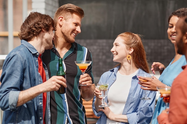 Portrait of two young men enjoying drinks at outdoor party with friends in sunlight