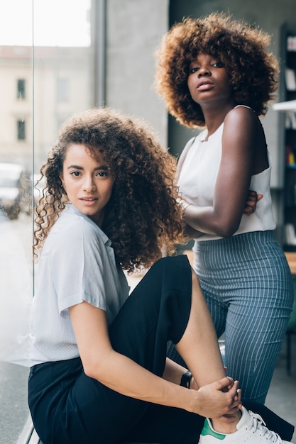 Portrait of two young multiracial and curly women posing together and looking