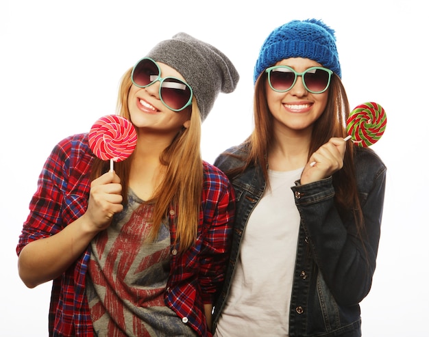 Portrait of two young pretty hipster girls wearing hats and sunglasses holding candys