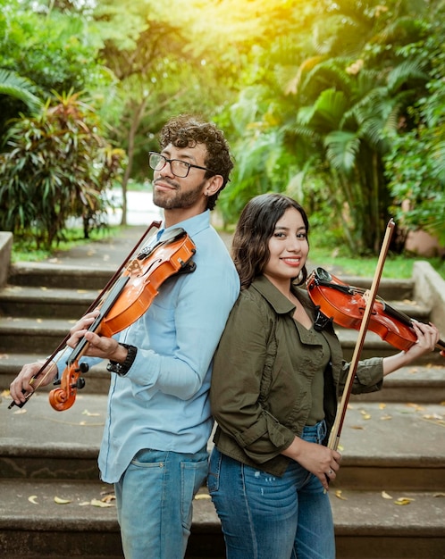 Portrait of two young violists back to back outdoors Portrait of smiling male and female violinist back to back outdoors Two young violinists back to back holding their violins