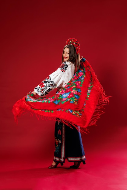 Portrait of ukrainian woman in traditional ethnic clothing and floral red wreath on viva magenta studio background twirls a handkerchief Ukrainian national embroidered dress call vyshyvanka