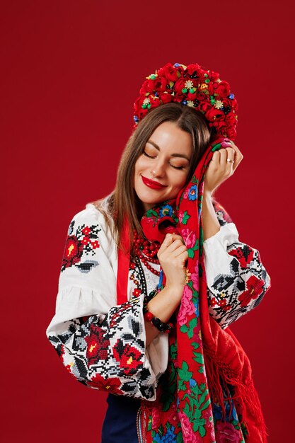 Portrait of ukrainian woman in traditional ethnic clothing and floral red wreath with handkerchief on viva magenta studio background Ukrainian national embroidered dress call vyshyvanka