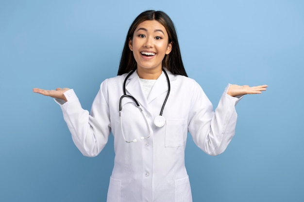 Portrait of uncertain asian woman doctor wearing white gown with raised arms