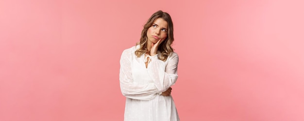 Portrait of uneasy thoughtful seriouslooking blond girl wear white dress look up lean head on palm a