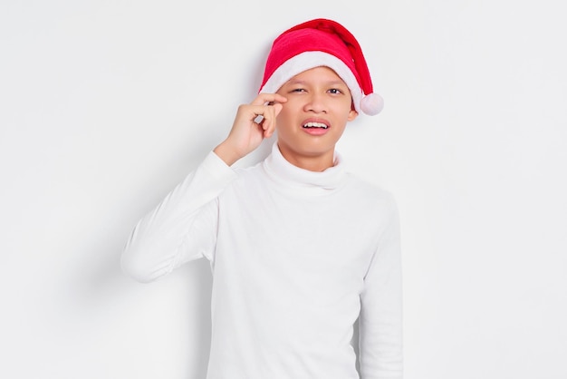 Portrait of unhappy Asian male in christmas hat rubs tears wants to cry feels depressed has a problem isolated on white background