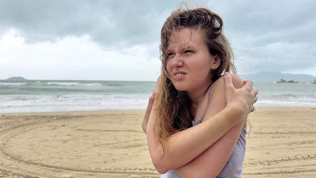 Portrait of unhappy depressed frozen trembling girl young shivering from cold sad upset woman on the sea beach bad weather on summer vacation