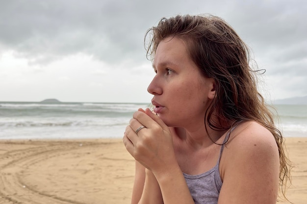 Portrait of unhappy depressed frozen trembling girl young shivering from cold sad upset woman on the sea beach bad weather on summer vacation