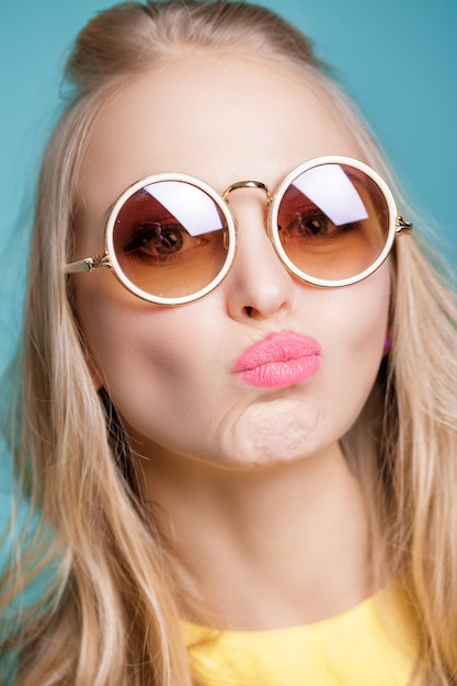 Portrait of unhappy and frustrated blond woman in sunglasses and yellow shirt on blue background