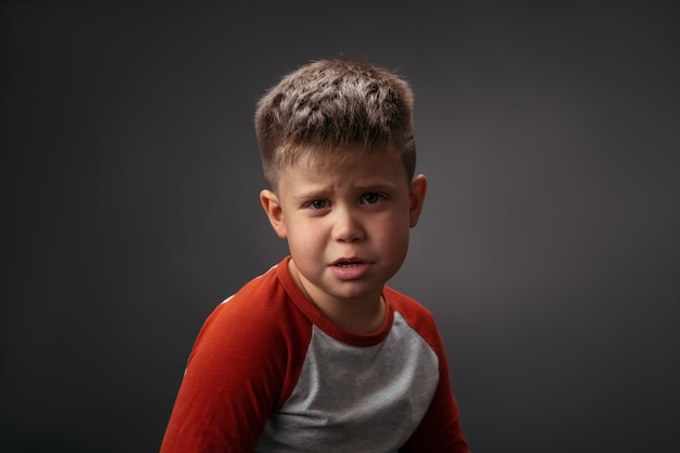 Portrait of a unhappy little boy sitting in the chair of the turn isolated on a grey dark background