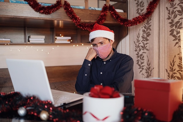 Portrait of unhappy man in mask sitting in room near christmas decorations