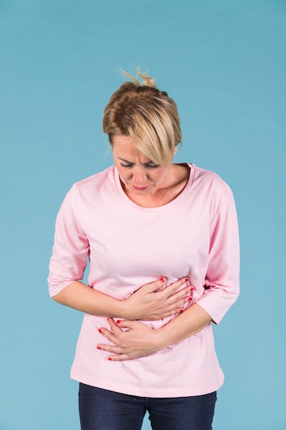 Portrait of a unhappy woman with abdominal pain on blue backdrop