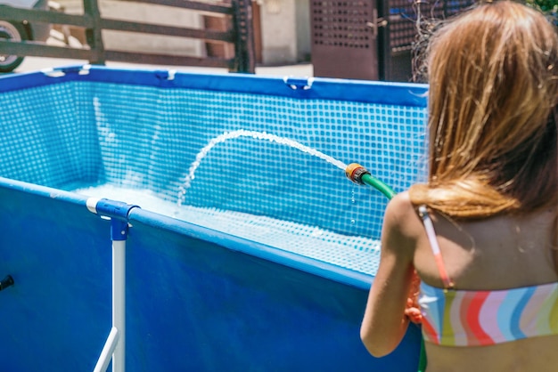 Portrait of an unrecognizable blonde girl filling the pool of the vacation cottage with a hose