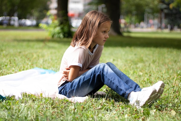 Portrait of an upset frustrated girl sitting on the grass touching her stomach, suffering