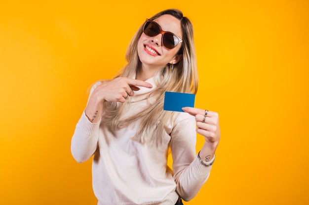 Portrait of very young woman pointing finger at credit card isolated on yellow background.