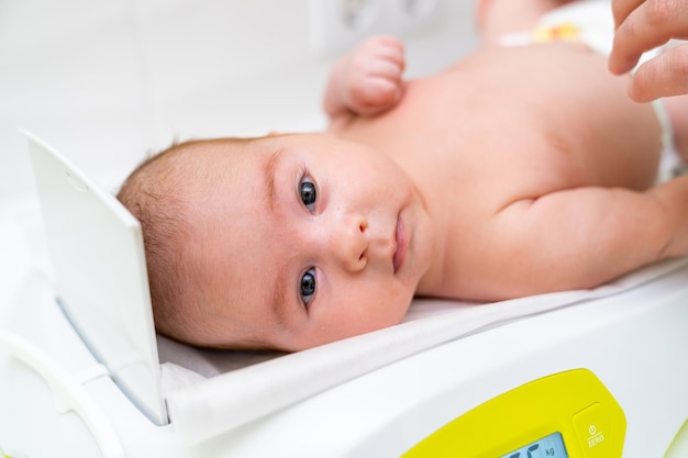 Portrait view of the little curious infant laying at the weight while having check up at the clinic