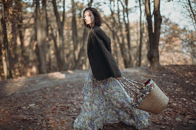 Portrait of vintage dressed young woman with basket of flowers walking in autumn park