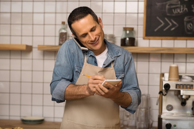 Portrait of waiter taking notes and talking on smartphone in cafe