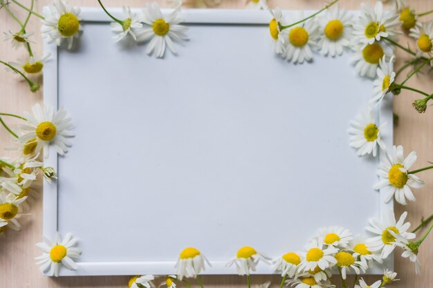 Portrait white picture frame mockup on wooden table glass vase with camomile