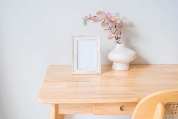 Portrait white picture frame mockup on wooden table. Modern ceramic vase with eucalyptus.