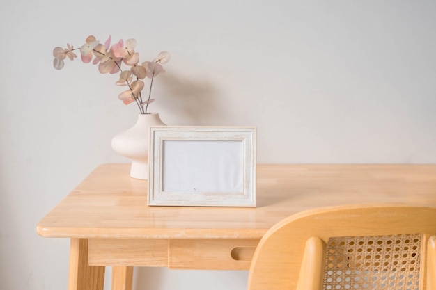 Portrait white picture frame mockup on wooden table. Modern ceramic vase with eucalyptus.