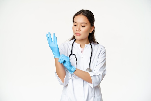 Portrait of woman asian doctor puts on rubber gloves to examine patient in clinic standing in health...