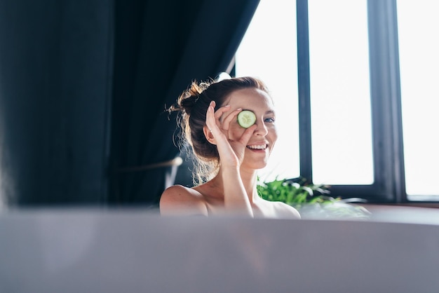 Portrait of a woman in a bathtub with a piece of cucumber before applying it to her face