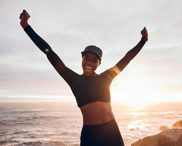 Photo portrait of woman celebrate by ocean for fitness in nature for exercise marathon training and running goals sports sunset and female person with hands in air for winning workout and wellness