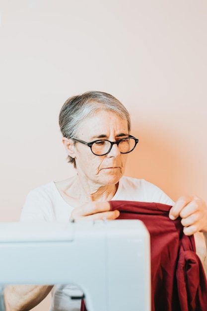 Portrait of woman clothes sewer in preparing the textiles to work on a machine elderly dressmaker cutting piece of cloth while working in workshop working old sewing machine technology of the past