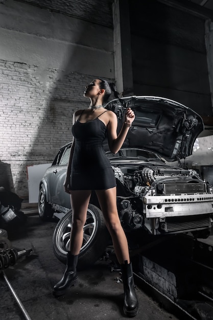 Portrait woman in  dress posing next to a  car in the garage.