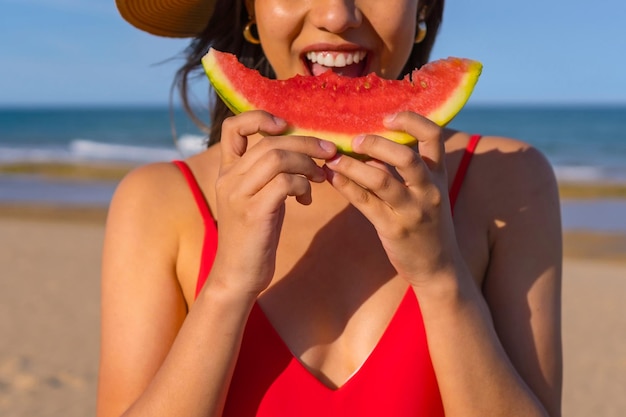 Portrait of a woman eating a watermelon by the beach Cutout of mouth smiling with red bikini