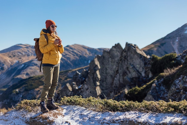 Portrait of a woman hiker standing with cup f tea on the slope of mountain ridge against mountains