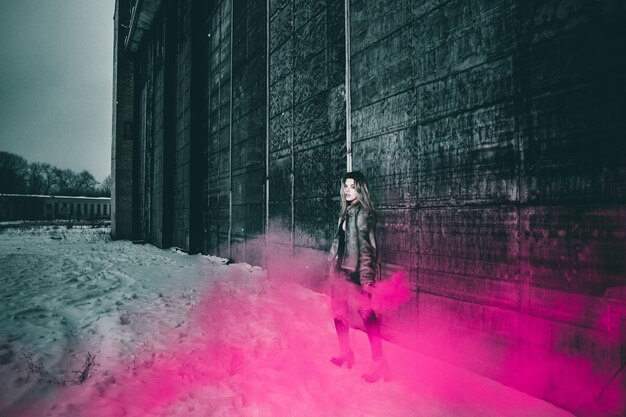 Photo portrait of woman holding distress flare while standing by building during winter